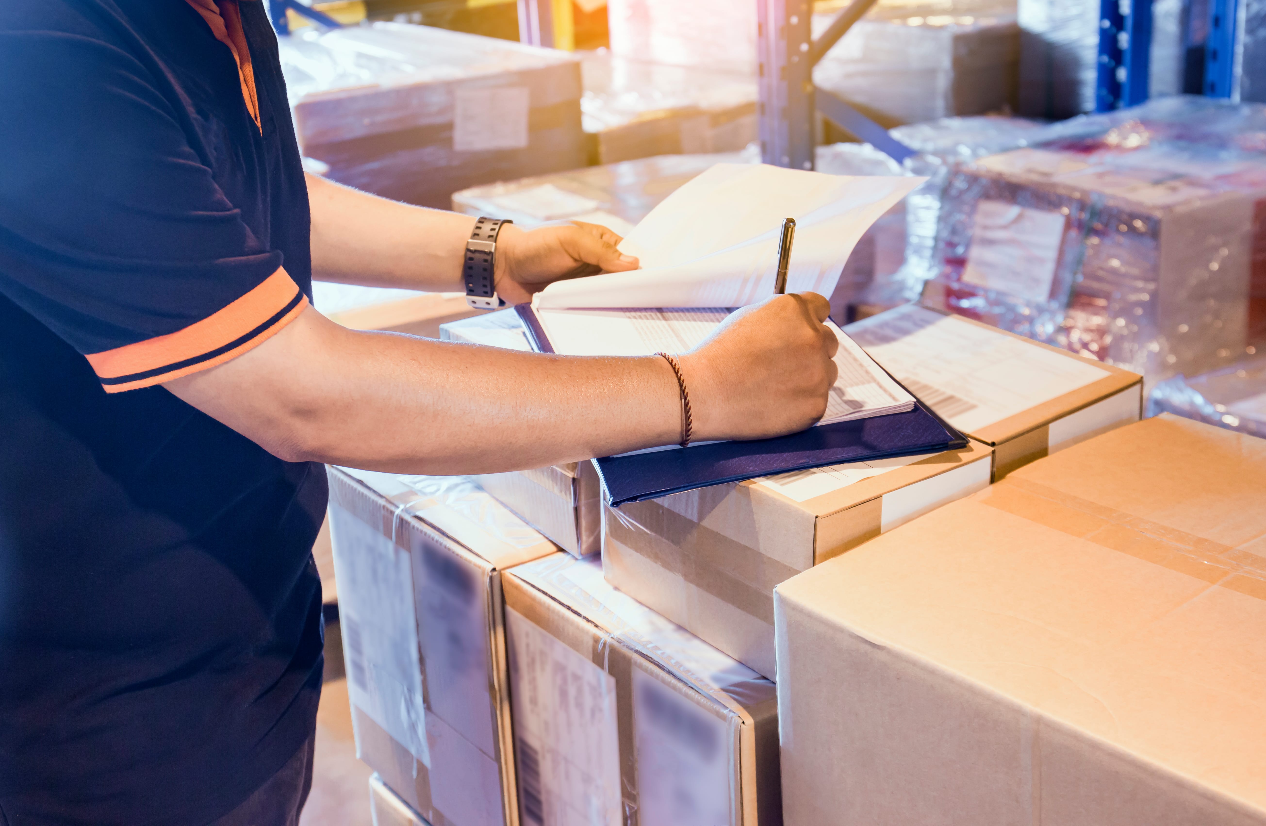 Warehouse worker writing on clipboard his checking details shipm Your Operations, Our Priority